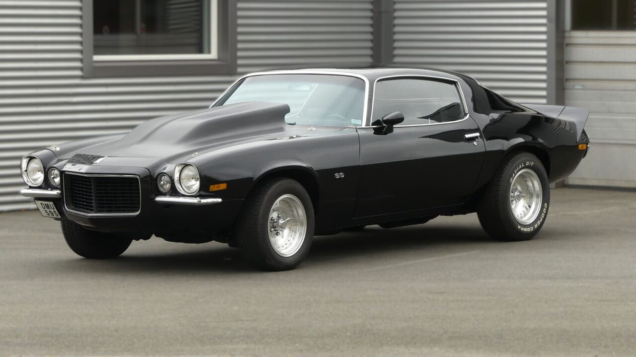 Svart Chevrolet Camaro SS 350 454 parkerad framför en byggnad med metallfasad